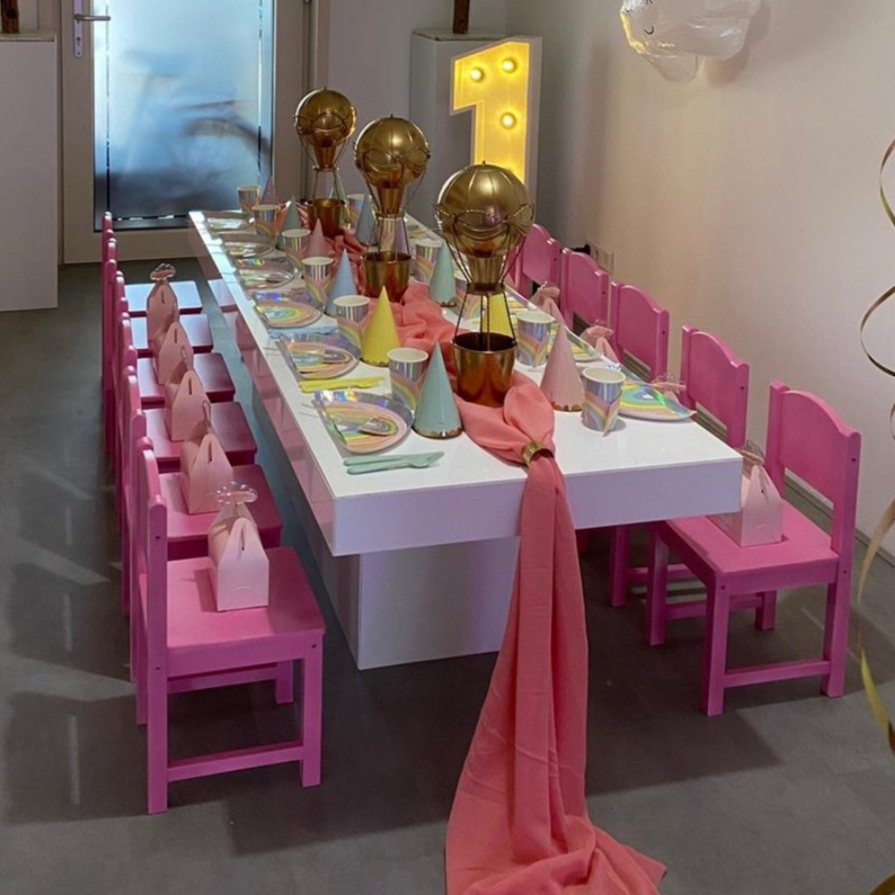 Kinderfeesttafel met roze stoelen en gouden ballonnen.