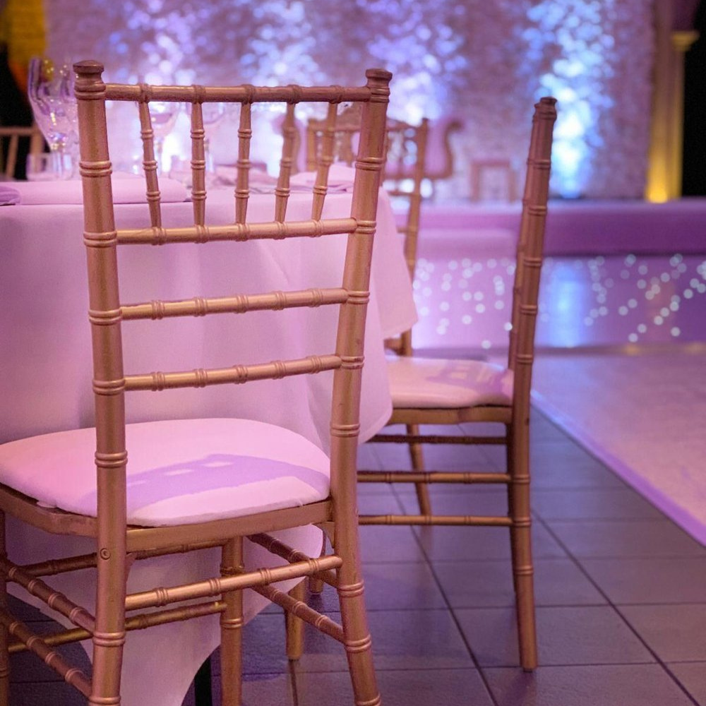 Bruiloftdecoratie met gouden stoelen en paarse verlichting.
