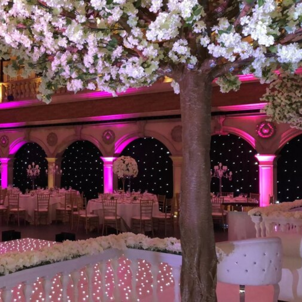 Feestzaal met gedecoreerde tafels en bloemenboom.
