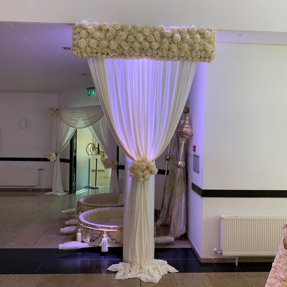 Feestelijke zaal met decoratieve witte gordijnen en bloemen.