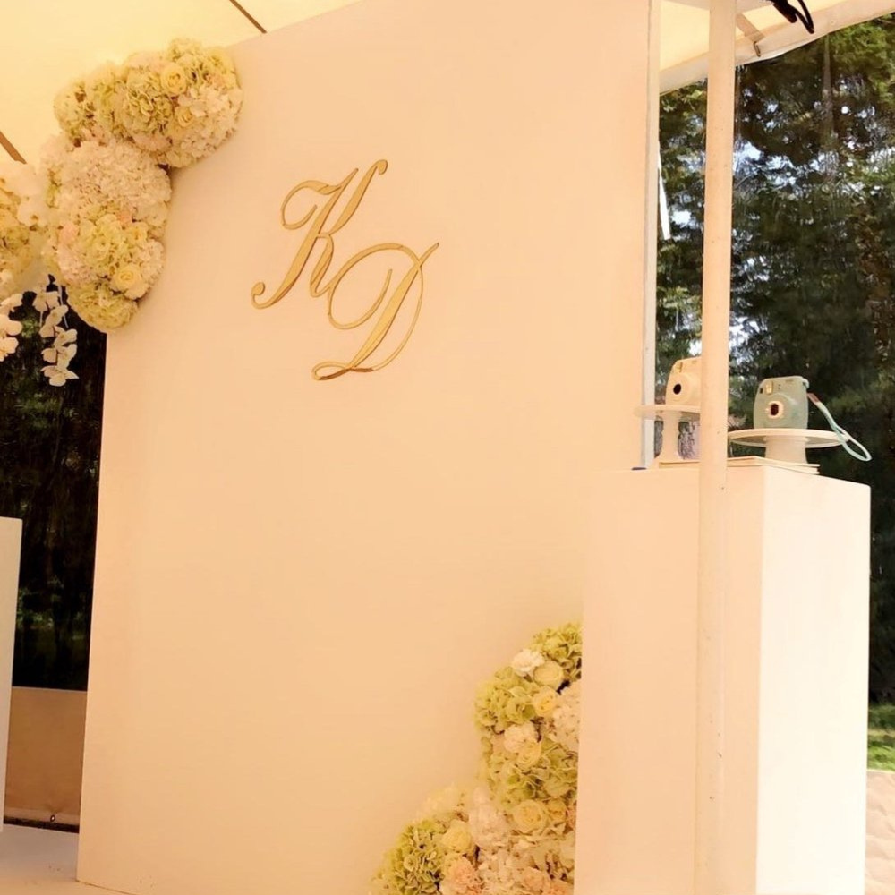 Witte muur met bloemen en gouden letters KD.
