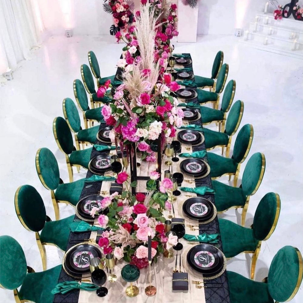 Elegante tafelopstelling met bloemen en groenfluwelen stoelen.
