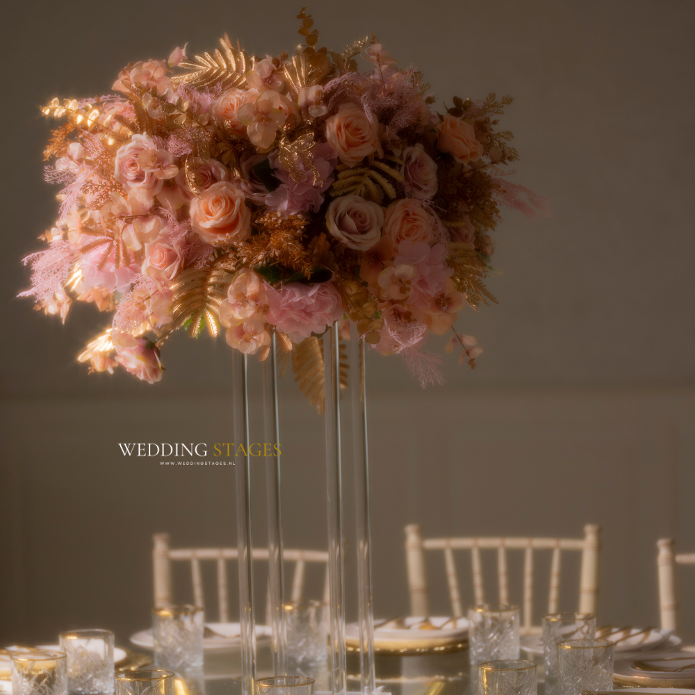 Hoge bloemenvaas met roze en gouden bloemstuk.