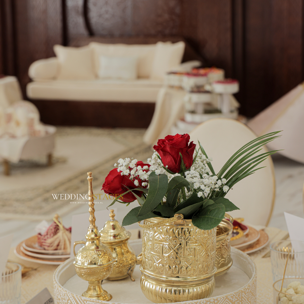 Gouden decoratie met rode rozen op trouwtafel.